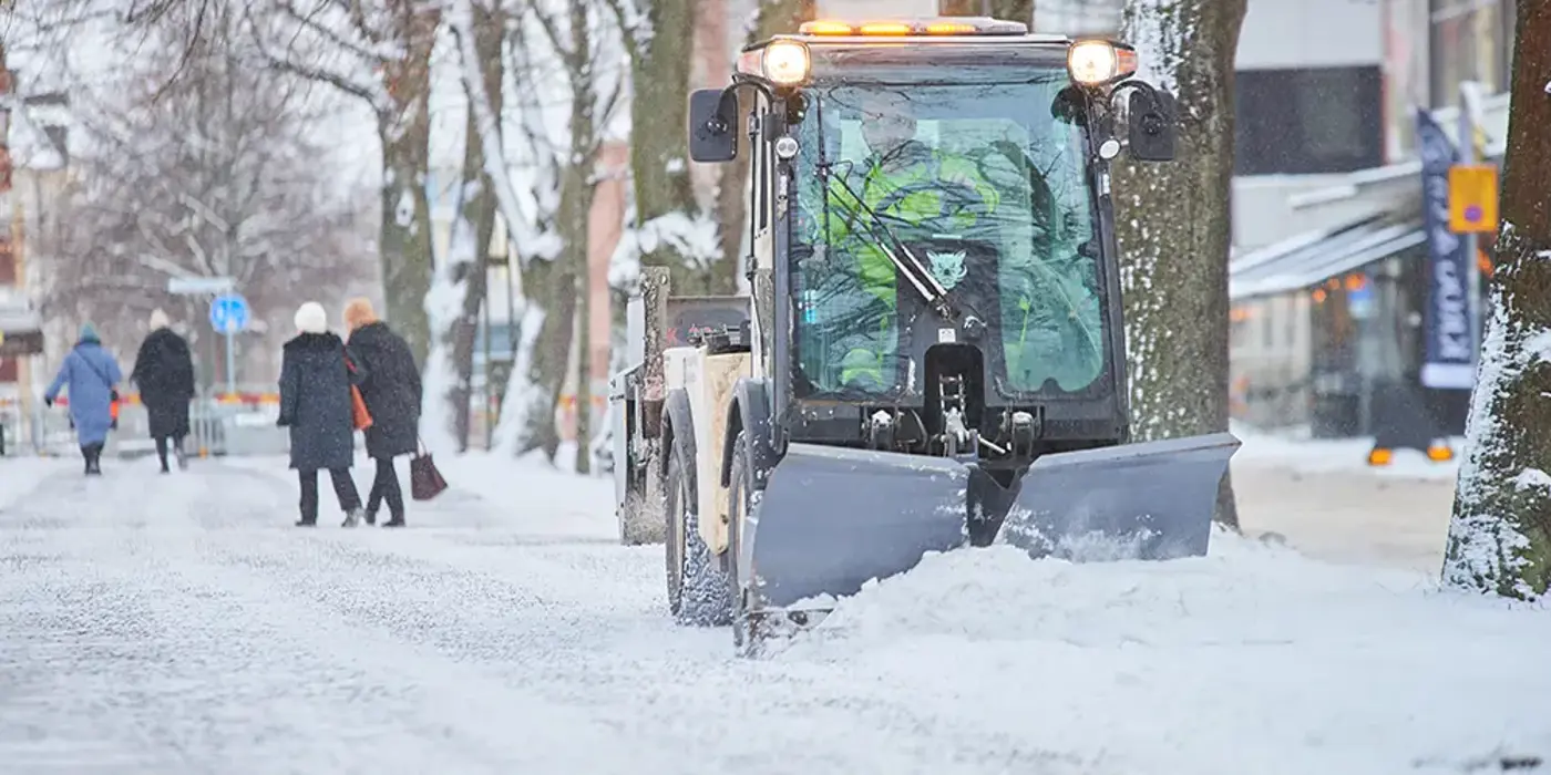 Snöplog röjer undan snö på en gångbana i stadsmiljö.