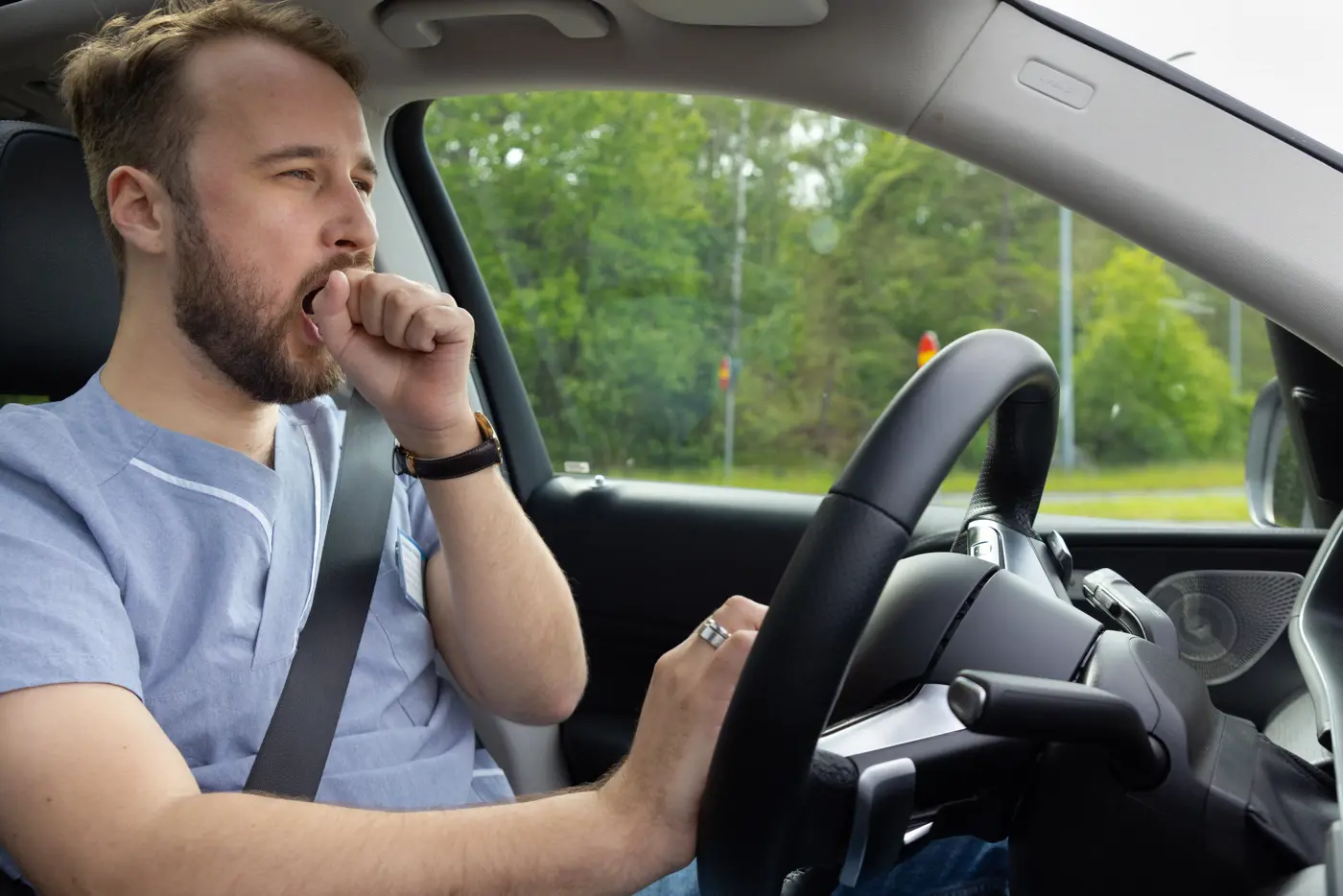 En person som arbetar inom vården kör bil och gäspar.