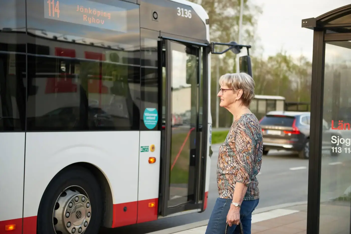 Äldre kvinna vid en busshållplats där en buss står