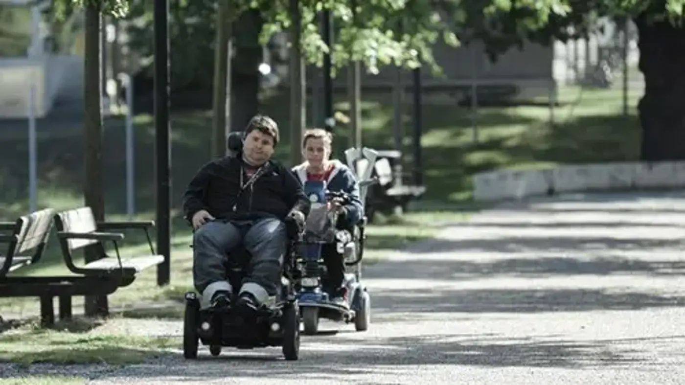 Två vuxna som kör elrullstol på en gångbana