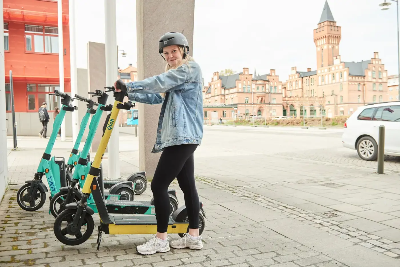 Tjej ståendes vid elsparkcykel med cykelhjälm.